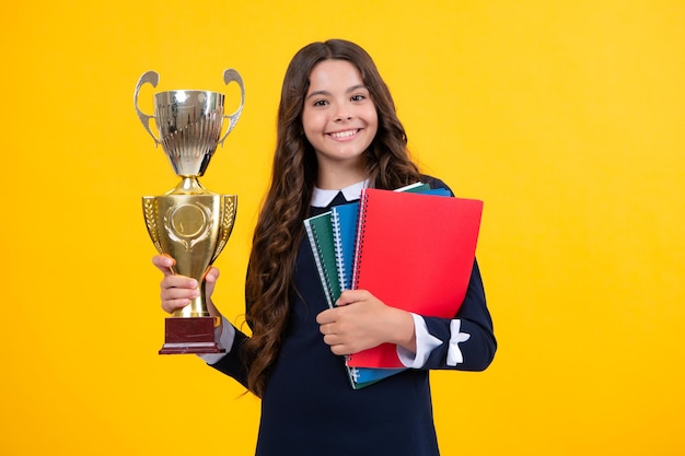 Schoolmeisje in schooluniform overwinning vieren met trofee Tiener met winnende prijs op gele achtergrond Schooljongen wint gouden trofee