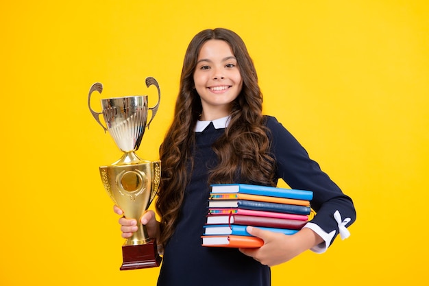 Schoolmeisje in schooluniform overwinning vieren met trofee Tiener met winnende prijs op gele achtergrond Schooljongen wint gouden trofee