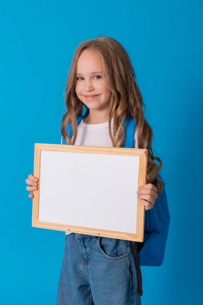 schoolmeisje in spijkerbroek en een wit T-shirt met een rugzak houdt een wit schrijfbord in haar handen