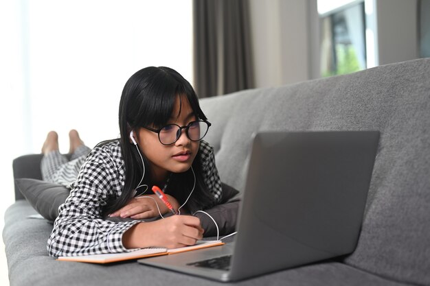 Schoolmeisje kijken naar les online en studeren vanuit huis met laptopcomputer. Concept van onderwijs op afstand.