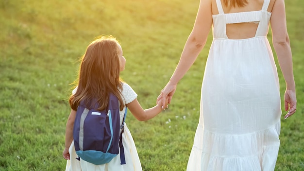 Schoolmeisje met blauwe rugzak gaat naar huis met moederhand