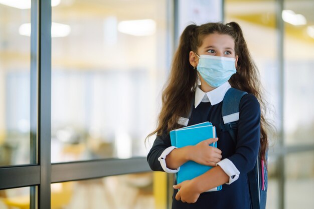 Schoolmeisje met een beschermend masker met een rugzak en een leerboek.