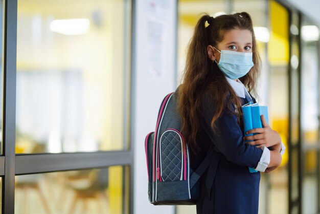 Schoolmeisje met een beschermend masker met een rugzak en een leerboek.