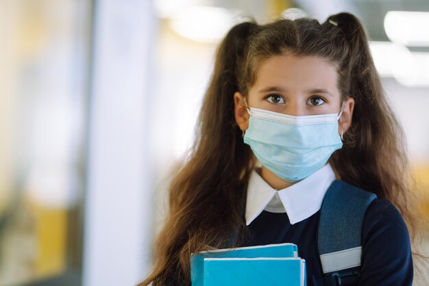 Schoolmeisje met een beschermend masker met een rugzak en een leerboek