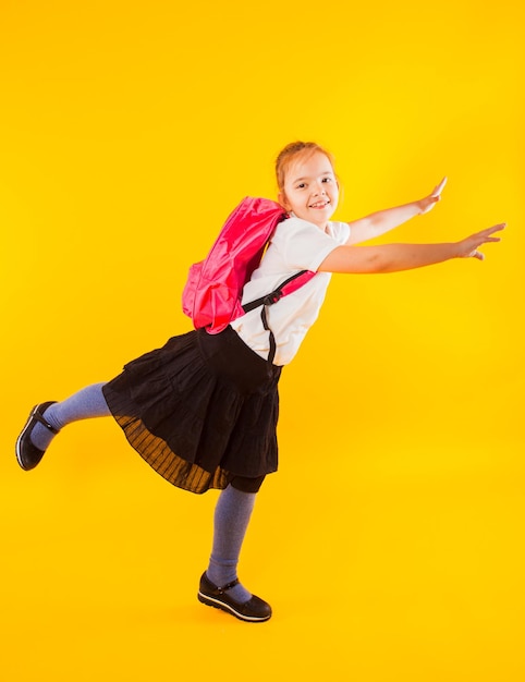 Schoolmeisje met een rugzak tijdens het springen op een gele achtergrond