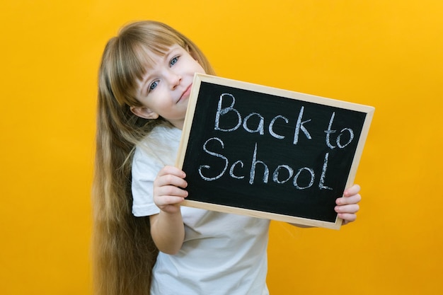 Schoolmeisje met een tablet in haar handen met de inscriptie Terug naar school op een gele achtergrond