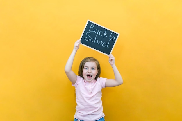 Schoolmeisje met een tablet in haar handen met de inscriptie Terug naar school op een gele achtergrond