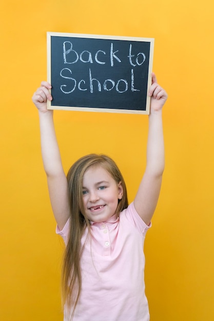 Schoolmeisje met een tablet in haar handen met de inscriptie Terug naar school op een gele achtergrond