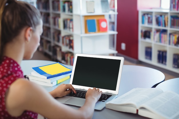 Schoolmeisje met laptop in bibliotheek