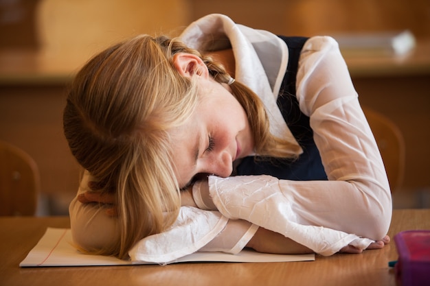 Schoolmeisje slaapt op het bureau tijdens de saaie les