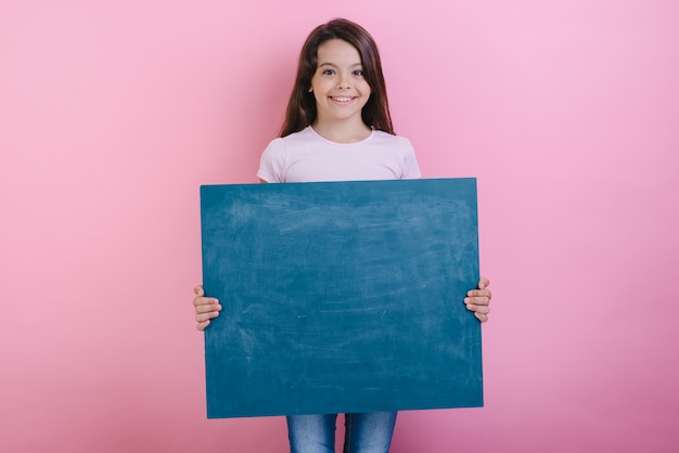 Schoolmeisje staat met een schoolbord in haar handen.