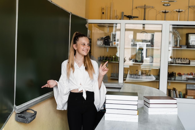 Schoolmeisje wijst met de vinger naar de rechterkant en glimlacht Schoolonderwijs Kind op school met veel boeken op blackboard