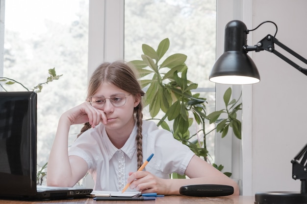 Schoolmeisje zelfisolatie met behulp van laptop voor zijn huiswerk. Gaming, onderwijs en school concept - verdrietig meisje met laptop en thuis. Meisje heeft het moeilijk om online huiswerk te maken, zit depressief binnenshuis