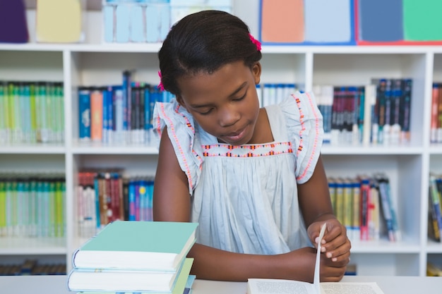 Schoolmeisje zittend op tafel en leesboek in bibliotheek