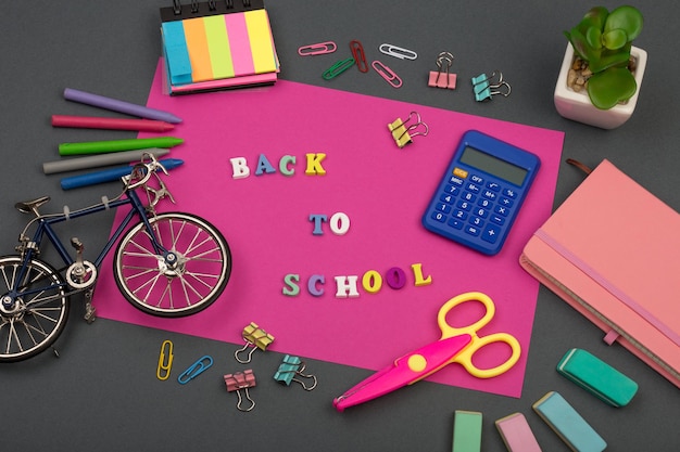 Schoolset met roze papieren tekst Terug naar school van houten letters fietsmodel rekenmachine kleurpotloden schaar notitieblok en ander briefpapier