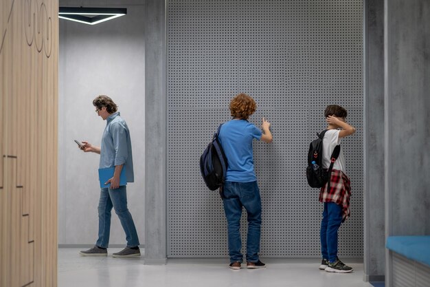 Schoolteacher with the cellphone and pupils in the school lobby