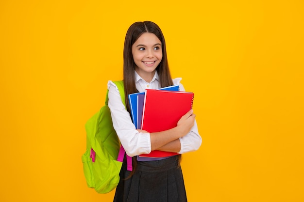 Schooltienermeisje met schooltasrugzak houdt boek op gele geïsoleerde studioachtergrond