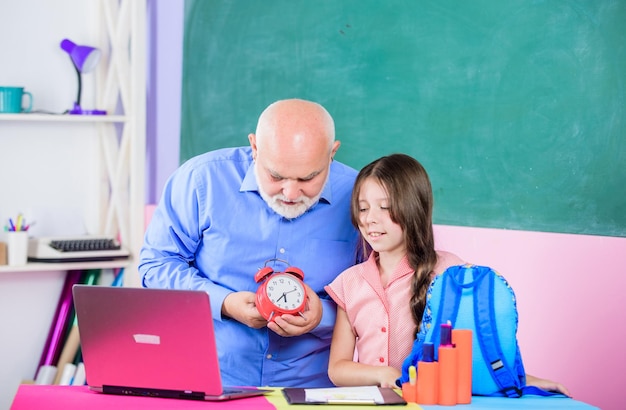 Schooltijd volwassen leraar help leerling met kloktijd om schoolles online te studeren klein meisje met man tutor studie op computer pauze alarm Ochtendonderwijs bloggen Terug naar school