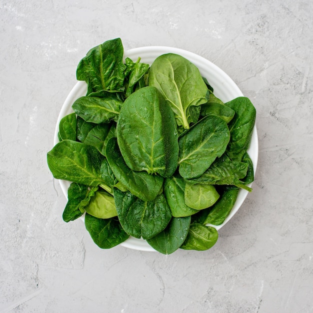 Schoon voedselconcept. Bladeren van verse biologische spinazie greens in een plaat op een lichte achtergrond. Gezond detox lente-zomer dieet. Veganistisch rauw voedsel.