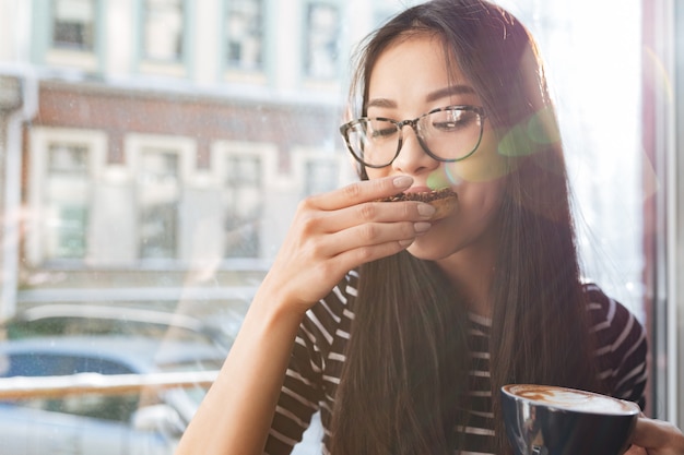 Schoonheid aziatische vrouw die cake op vensterbank eet