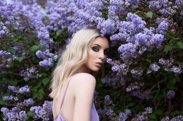 Schoonheid blonde vrouw in de zomer in een lila Bush. Schoonheidsportret van een meisje met paarse bloemen, mooie make-up