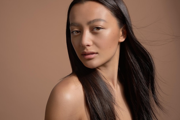 Schoonheid brunette model gemengd ras model met lang sterk steil haar waait Ideale huid natuurlijke make-up op beige achtergrond