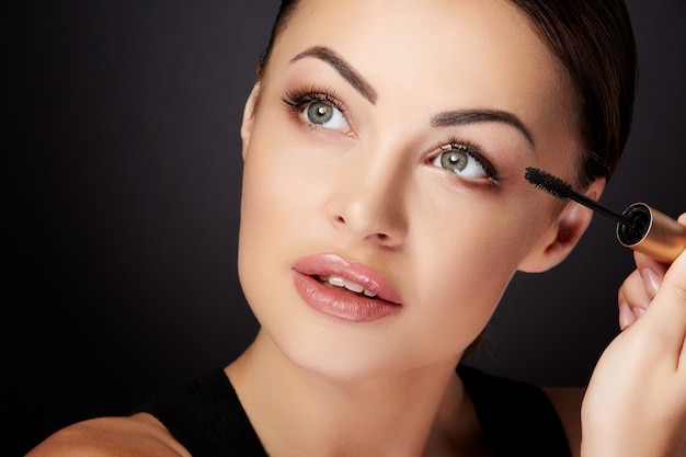 Foto schoonheid concept, vrouw met mascara. close-up, portret van vrouw opzoeken, wimpers met mascara schilderen. studio, binnen, zwarte achtergrond