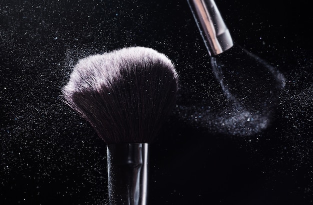 Schoonheid en make-up concept. De schoonheidsmiddelen borstelen het vrijgeven van een wolk van roze fonkelend gezichtspoeder over zwarte achtergrond.