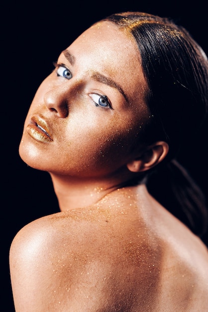 Schoonheid fashion art model meisje met gouden huid. Close-up portret van meisje met blauwe ogen op zwarte achtergrond