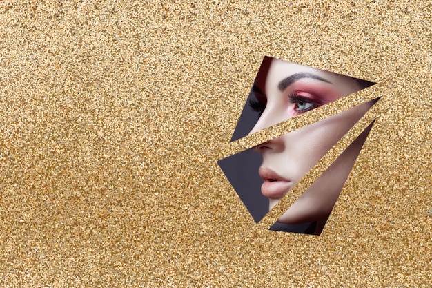 Schoonheid gezicht rode ogen make-up van een jong meisje in een spleet van geel goud papier. Vrouw met mooie make-up rode gloeiende schaduw, mollige lippen, grote ogen kleur in gouden spleet