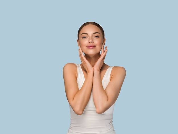 Schoonheid gezonde huid vrouwen aanraken van gezicht cosmetische studio portret. Sportkleding kleur achtergrond blauw