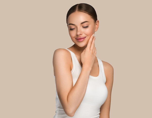 Schoonheid gezonde huid vrouwen aanraken van gezicht cosmetische studio portret. Sportkleding kleur achtergrond bruin