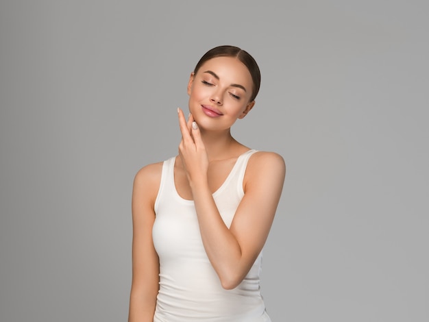 Schoonheid gezonde huid vrouwen aanraken van gezicht cosmetische studio portret. sportkleding kleur achtergrond grijs