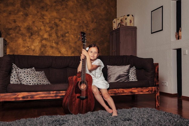 Schoonheid klein meisje in witte kleren met gitaar in het interieur van de woonkamer