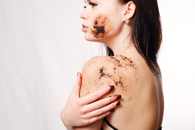 Schoonheid, mensen en gezond huidconcept - de donkerbruine vrouw reinigt huid van de lichaamskoffie scrub witte geïsoleerde achtergrond. Schoonheid portret. Beautiful Spa vrouw wat betreft haar gezicht. Perfecte frisse huid.