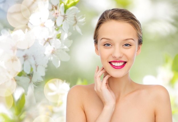 schoonheid, mensen en gezondheid concept - glimlachend jong vrouwengezicht met roze lippenstift op lippen en schouders over groene natuurlijke kersenbloesem achtergrond