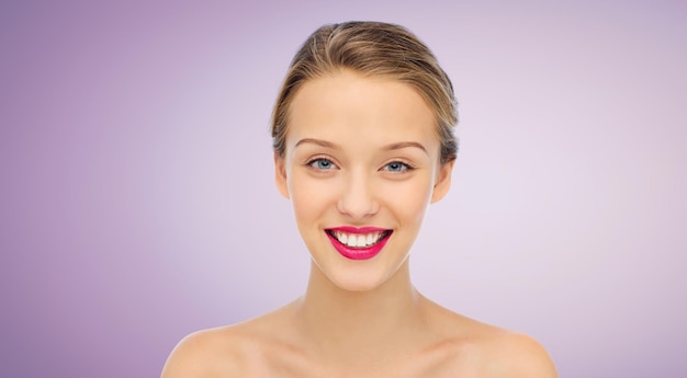 schoonheid, mensen en gezondheid concept - glimlachend jong vrouwengezicht met roze lippenstift op lippen en schouders over violette achtergrond