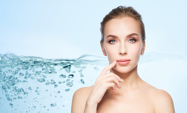 schoonheid, mensen en plastische chirurgie concept - mooie jonge vrouw die haar lippen laat zien over water splash bubbels op blauwe achtergrond