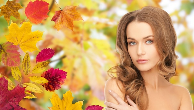 schoonheid, mensen, seizoen en gezondheidsconcept - mooi jong vrouwengezicht met lang krullend haar over de achtergrond van de herfstbladeren