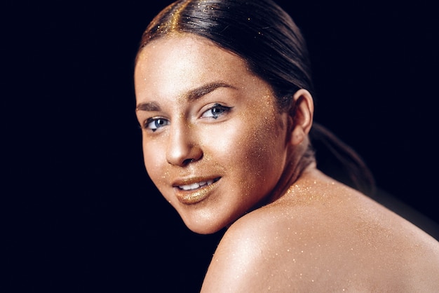 Schoonheid mode kunst model meisje met gouden huid. Close-up portret van meisje met blauwe ogen op zwarte achtergrond