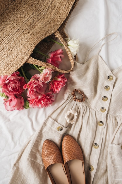 Schoonheid mode samenstelling met vrouwelijke zonnekleding sarafan, schoenen, roze pioenroos bloemen in strozak op linnen. Plat lag, bovenaanzicht