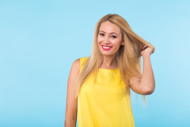 Schoonheid mode zomer portret van blonde vrouw met rode lippen en gele jurk op blauwe muur met kopie ruimte.