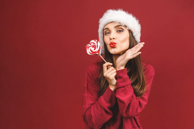 Schoonheid model meisje in kerstman hoed met rode lippen en xmas lollipop snoep wijzende hand