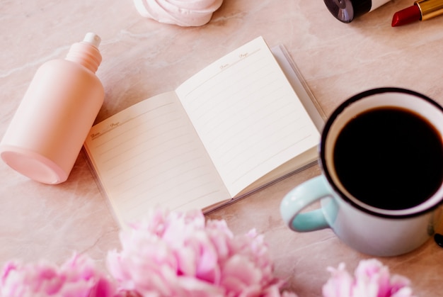 Schoonheid plat leggen met een dagboek, kopje koffie, accessoires en pioenrozen op een marmeren achtergrond