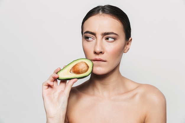 Schoonheid portret van een jonge gezonde aantrekkelijke brunette vrouw geïsoleerd, poseren met een gesneden avocado