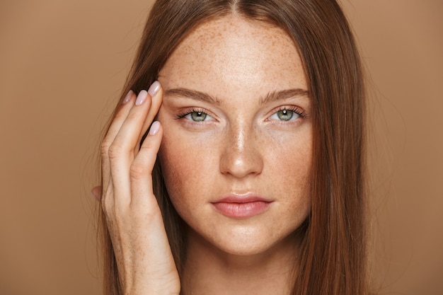 Schoonheid portret van een sensuele jonge topless vrouw met lang rood haar poseren, hand in hand op haar gezicht geïsoleerd over beige muur