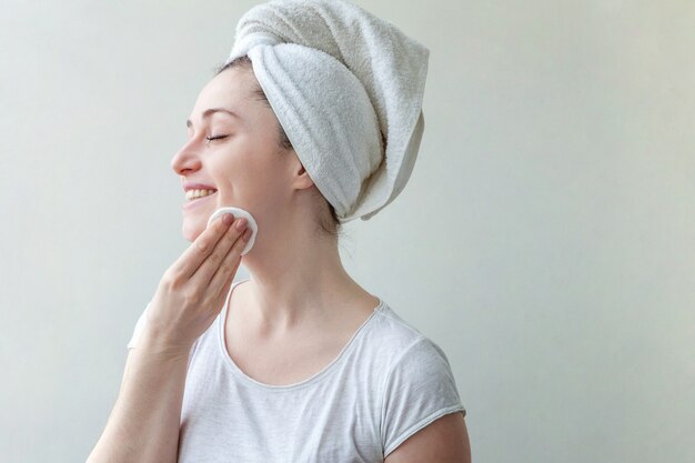 Schoonheid portret van lachende vrouw in handdoek op hoofd met zachte gezonde huid make-up verwijderen met wattenschijfje geïsoleerd op een witte achtergrond.