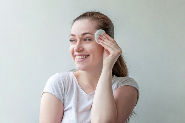 Schoonheid portret van lachende vrouw met zachte gezonde huid make-up verwijderen met wattenschijfje geïsoleerd op een witte achtergrond.