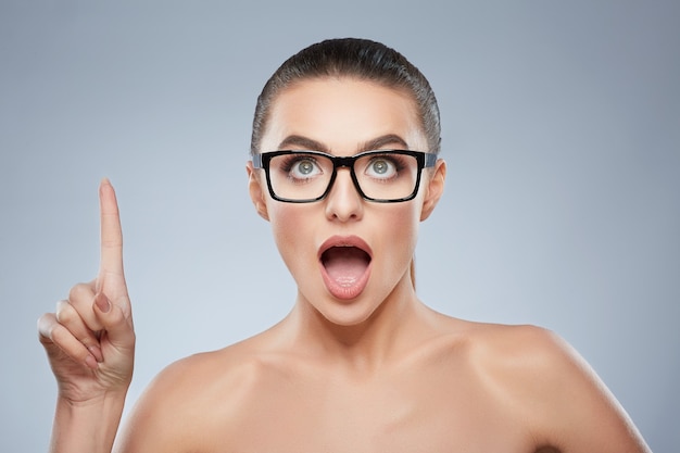 Schoonheid portret van meisje in glazen op zoek en omhoog met vinger. Hoofd en schouders van de vrouw die het idee heeft, sla het idee over. Natuurlijke make-up, studio, echte emoties tonen