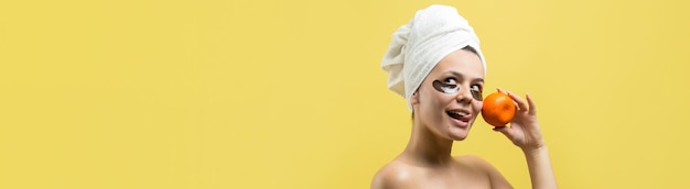 Schoonheid portret van vrouw in witte handdoek op hoofd met goud voedend masker op gezicht Huidverzorging reiniging eco organische cosmetische spa ontspannen concept Een meisje staat met haar rug met een oranje mandarijn